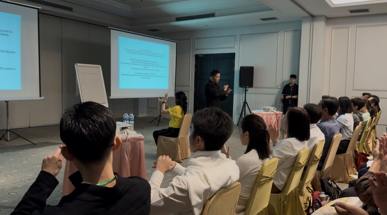 Fasilitator memandu peserta di depan layar presentasi